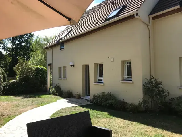 Maison couleur crème avec fenêtres, toit en pente et allée de jardin ensoleillée