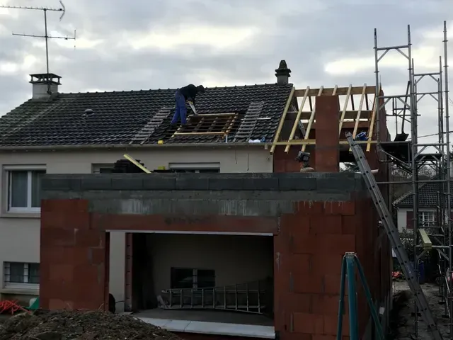 Toiture en rénovation avec ouvriers, échafaudages et nouvelle construction au-dessus d'un garage en briques rouges