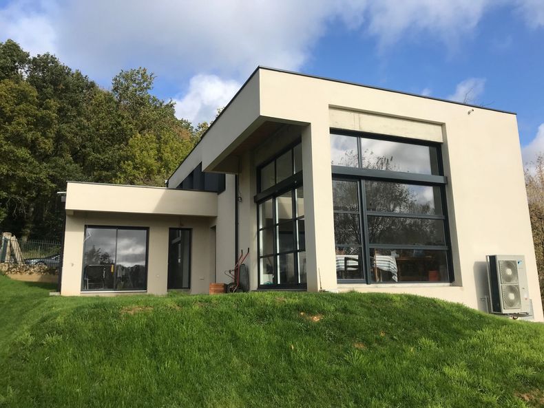 Maison moderne couleur crème avec de grandes fenêtres sur une colline herbeuse sous un ciel bleu