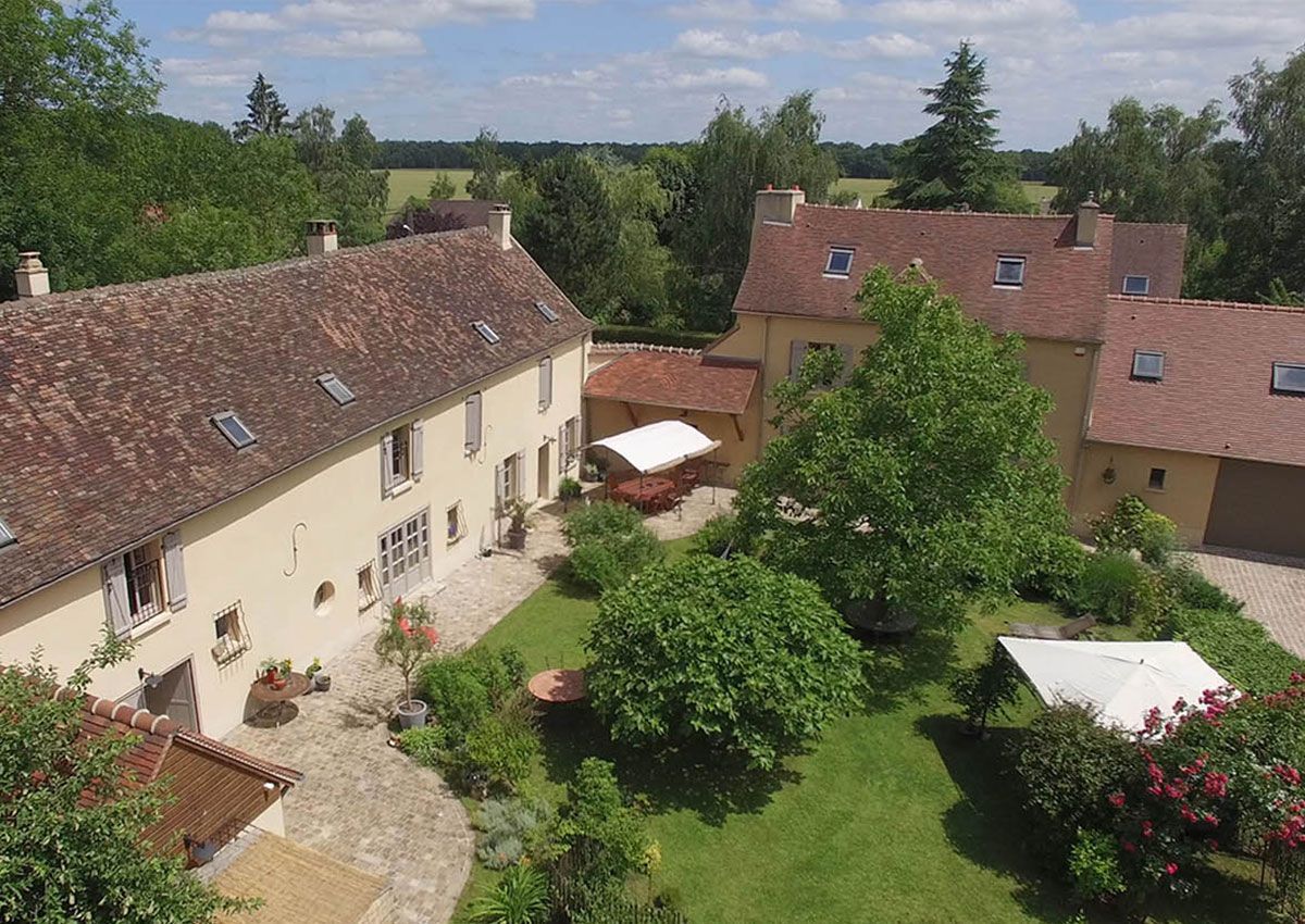 Vue aérienne d'une cour de campagne avec des bâtiments aux toits rouges, des arbres et des pelouses vertes.