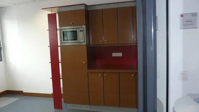 Pièce vide avec des placards intégrés marron, un micro-ondes et un panneau décoratif rouge près d'une porte.
