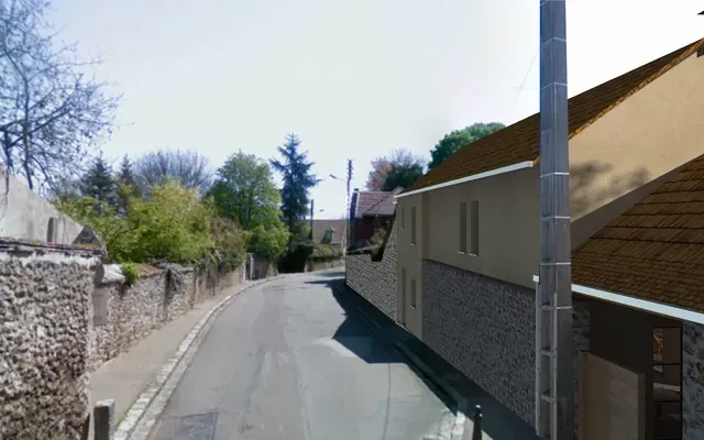 Rue étroite et tranquille, bordée d'un mur de pierre à gauche, de maisons à droite et d'un lampadaire sous un ciel dégagé.