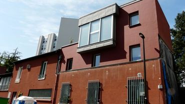 Bâtiment en briques rouges avec des fenêtres à barreaux et une façade supérieure moderne grise et bordeaux sous un ciel bleu