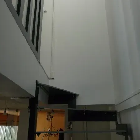 Cage d'escalier intérieure avec murs blancs, rampe noire et porte ouverte en dessous.
