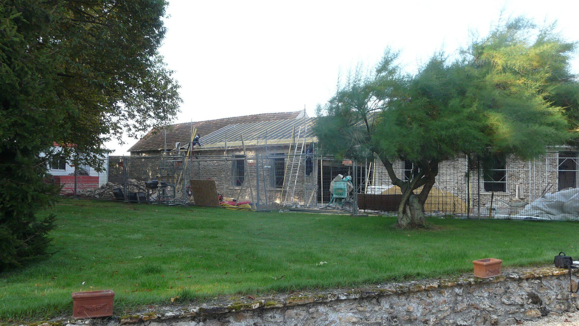 Ancien bâtiment en pierre au toit endommagé, entouré d'herbe verte et d'arbres