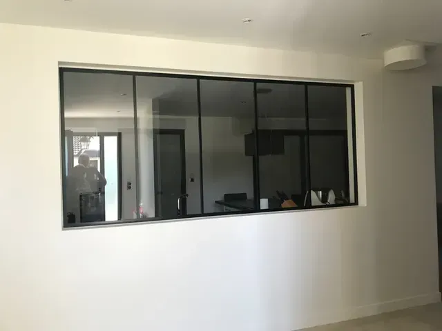 Mur intérieur avec une grande fenêtre à cadre noir donnant sur un bureau ou une salle de réunion