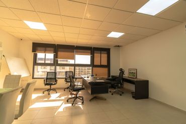 Bureau vide avec bureaux, chaises et grandes fenêtres laissant entrer la douce lumière du soleil.