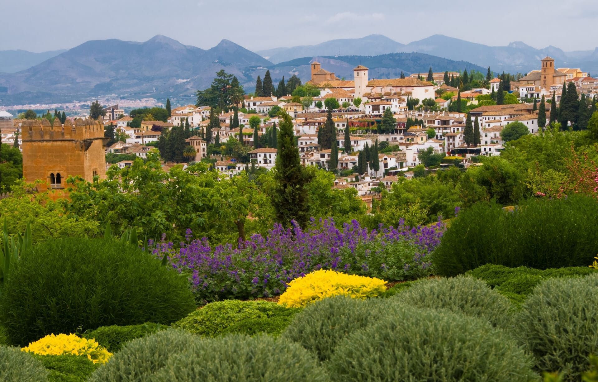 Jardín colorido con vistas a un pueblo en la ladera de una colina con montañas al fondo.
