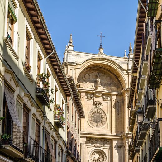 Calle estrecha flanqueada por edificios que conduce a una catedral de piedra ornamentada bajo un cielo azul.