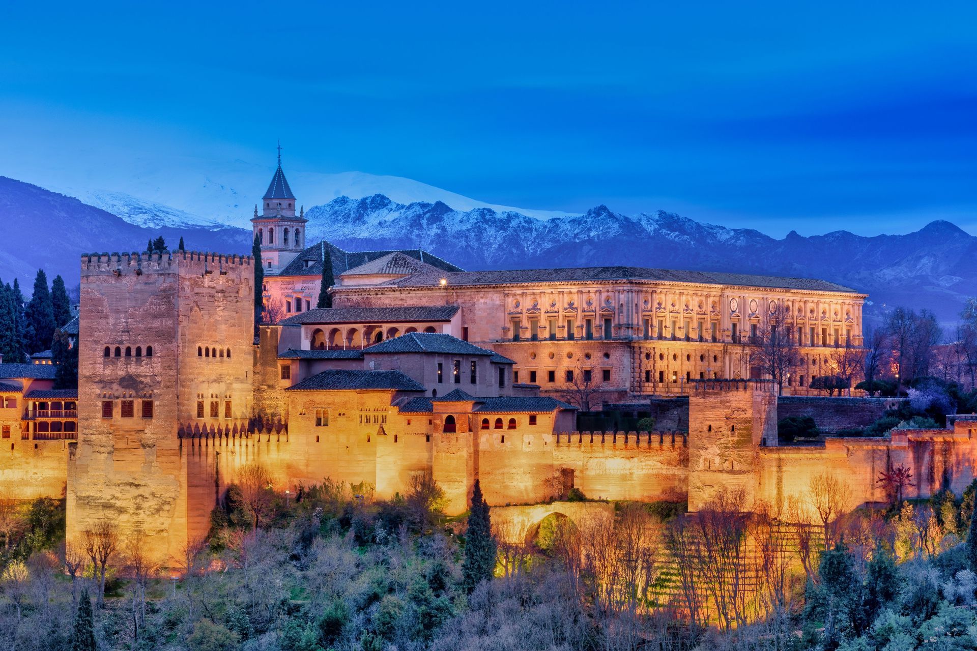 Castillo de piedra iluminado al atardecer con montañas al fondo.