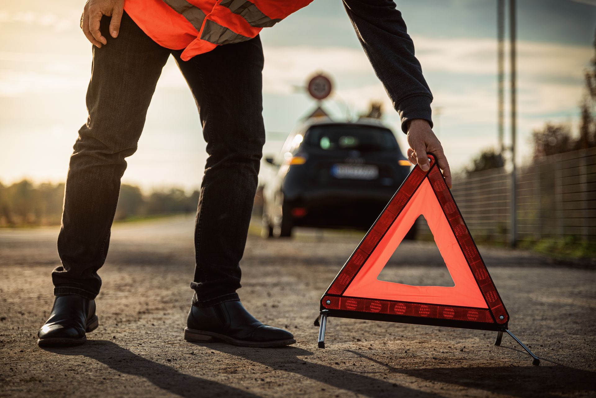 Un homme en gilet orange posant un triangle de signalisation devant une voiture