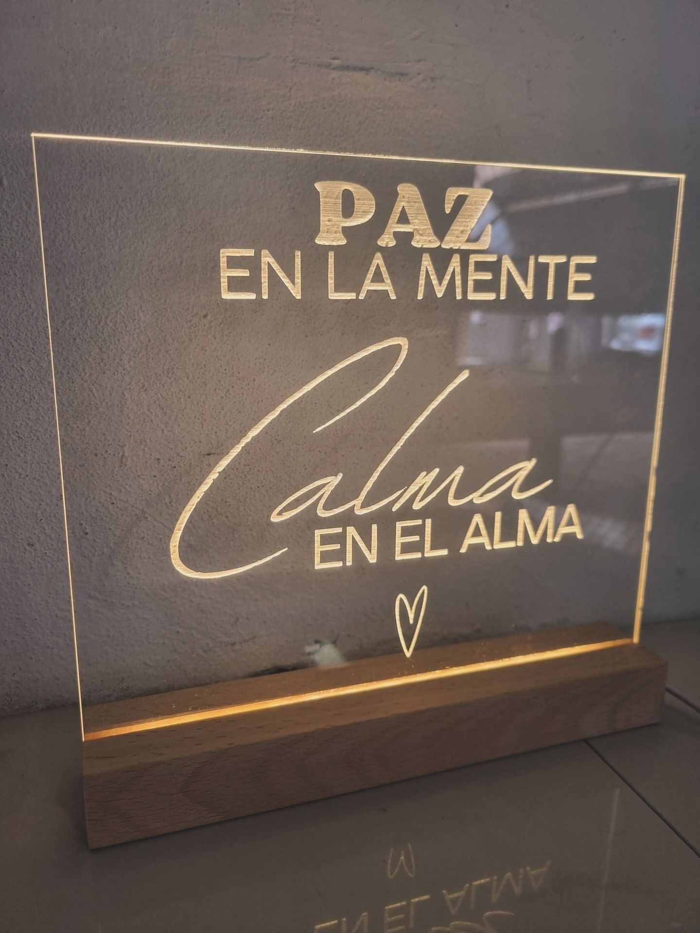 Letrero acrílico iluminado con texto en español: «Paz en la mente, calma en el alma». Base de madera.