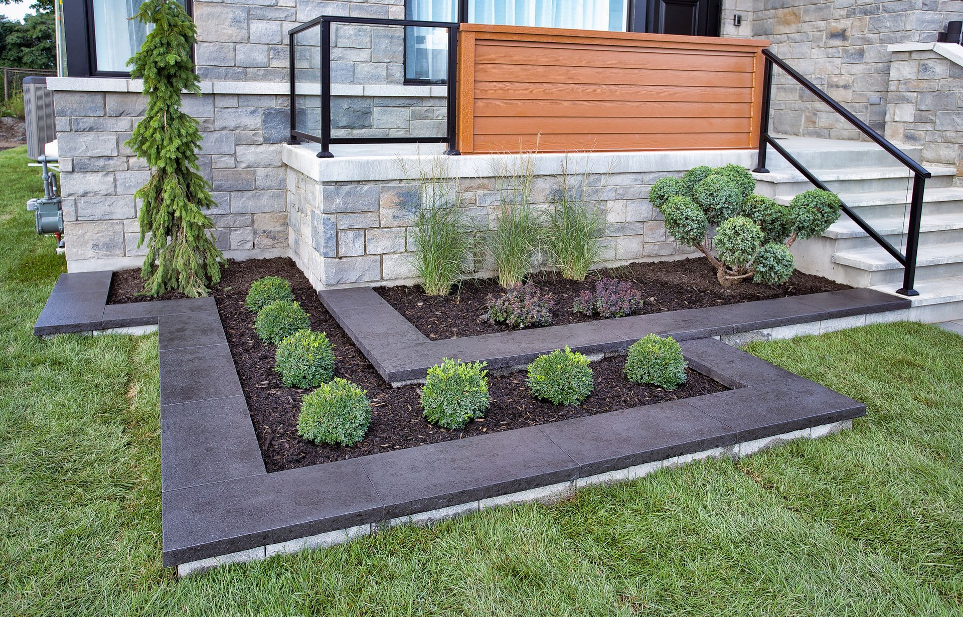 L'extérieur d'une maison moderne avec un aménagement paysager soigné, comportant une façade en pierre et de l'herbe vert foncé.