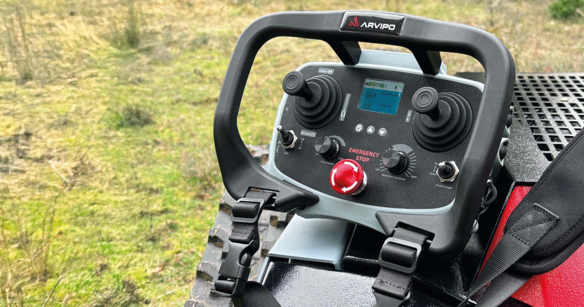 Télécommande de tondeuse robotisée sur chenilles dans un champ d'herbe.