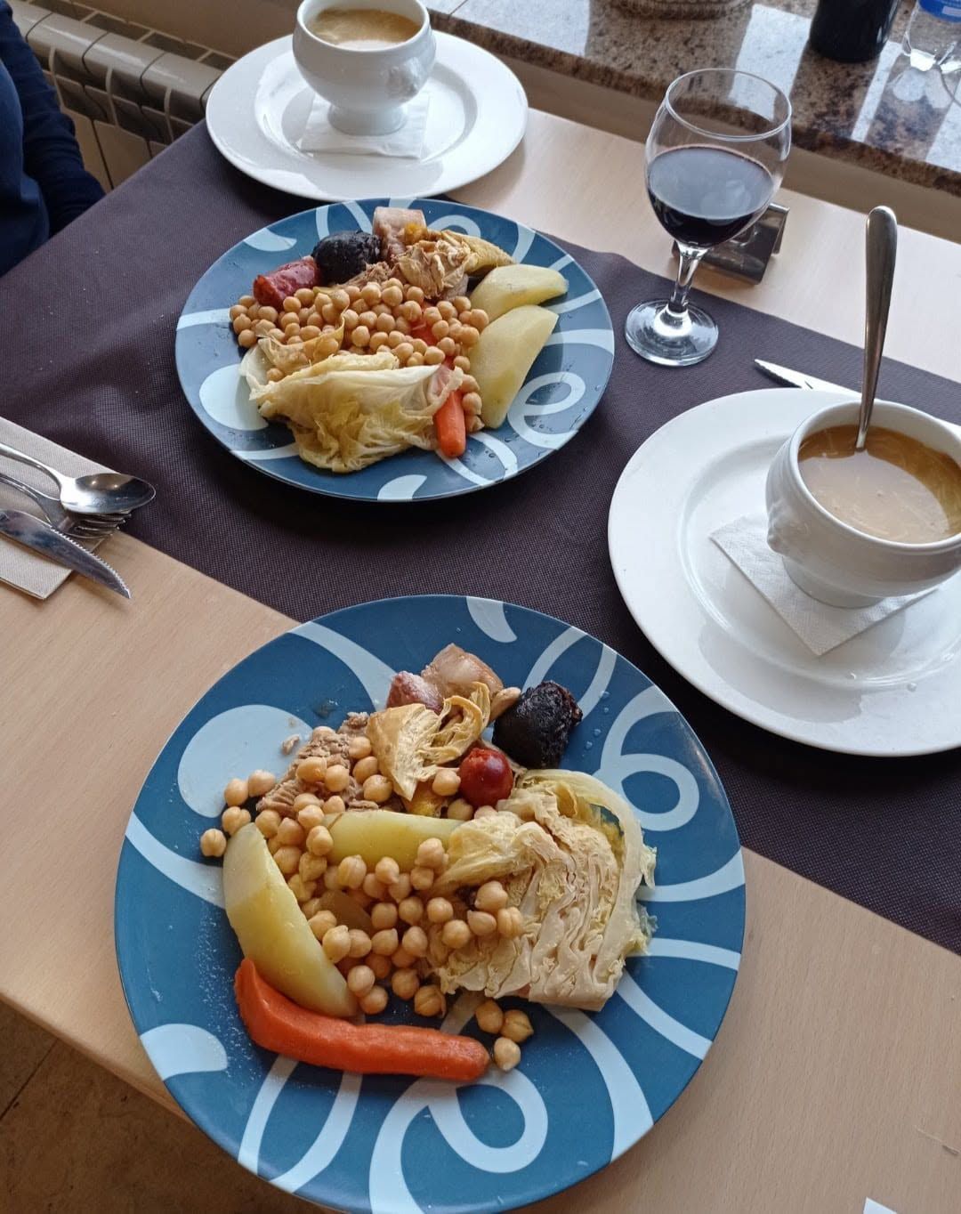 Dos platos de cuscús con garbanzos y verduras sobre una mesa de comedor con café y vino tinto.