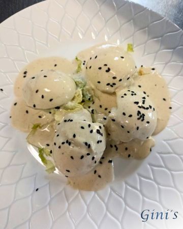 Bolitas de masa cremosa cubiertas con semillas de sésamo negro en un plato blanco.