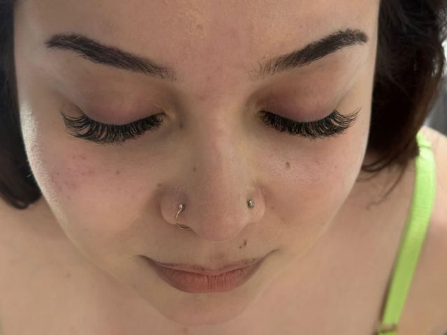 Primer plano de una persona mirando hacia abajo, con un piercing en la nariz y tiras de color verde brillante visibles.