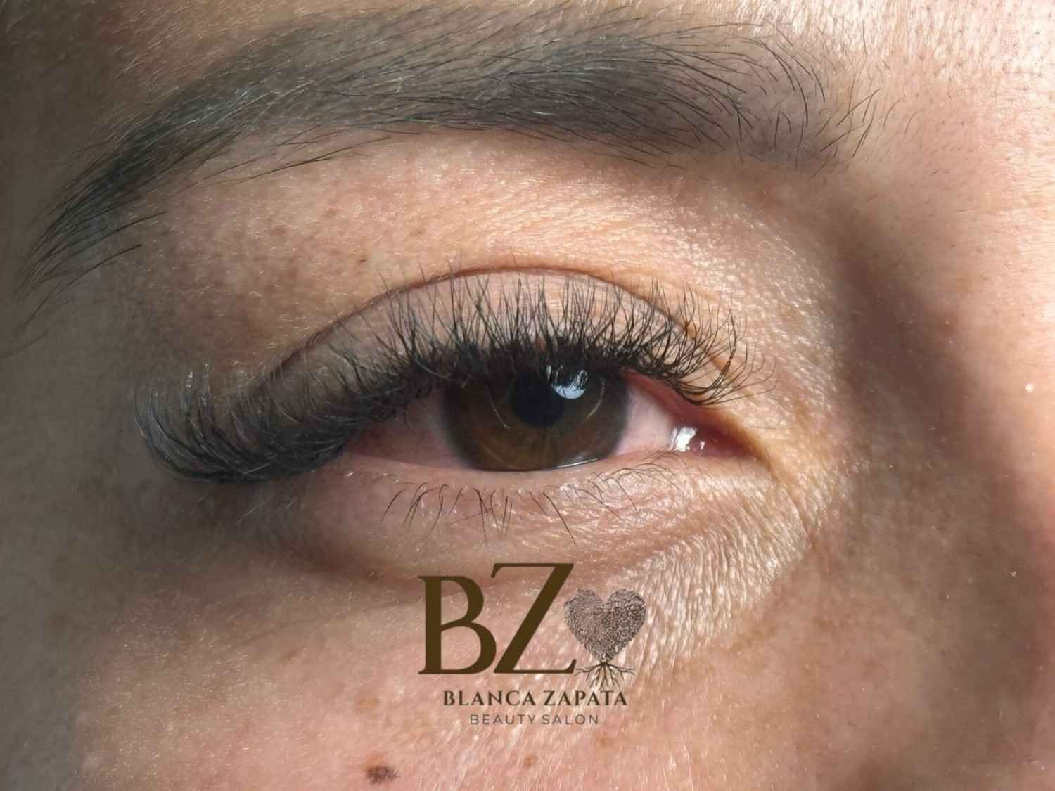 Primer plano del ojo de una mujer con pestañas largas y un maquillaje de ojos con sombra dorada.