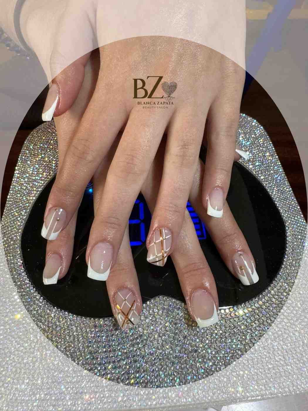 Manos con uñas decoradas con diseños blancos y brillantes sobre una superficie plateada reluciente.