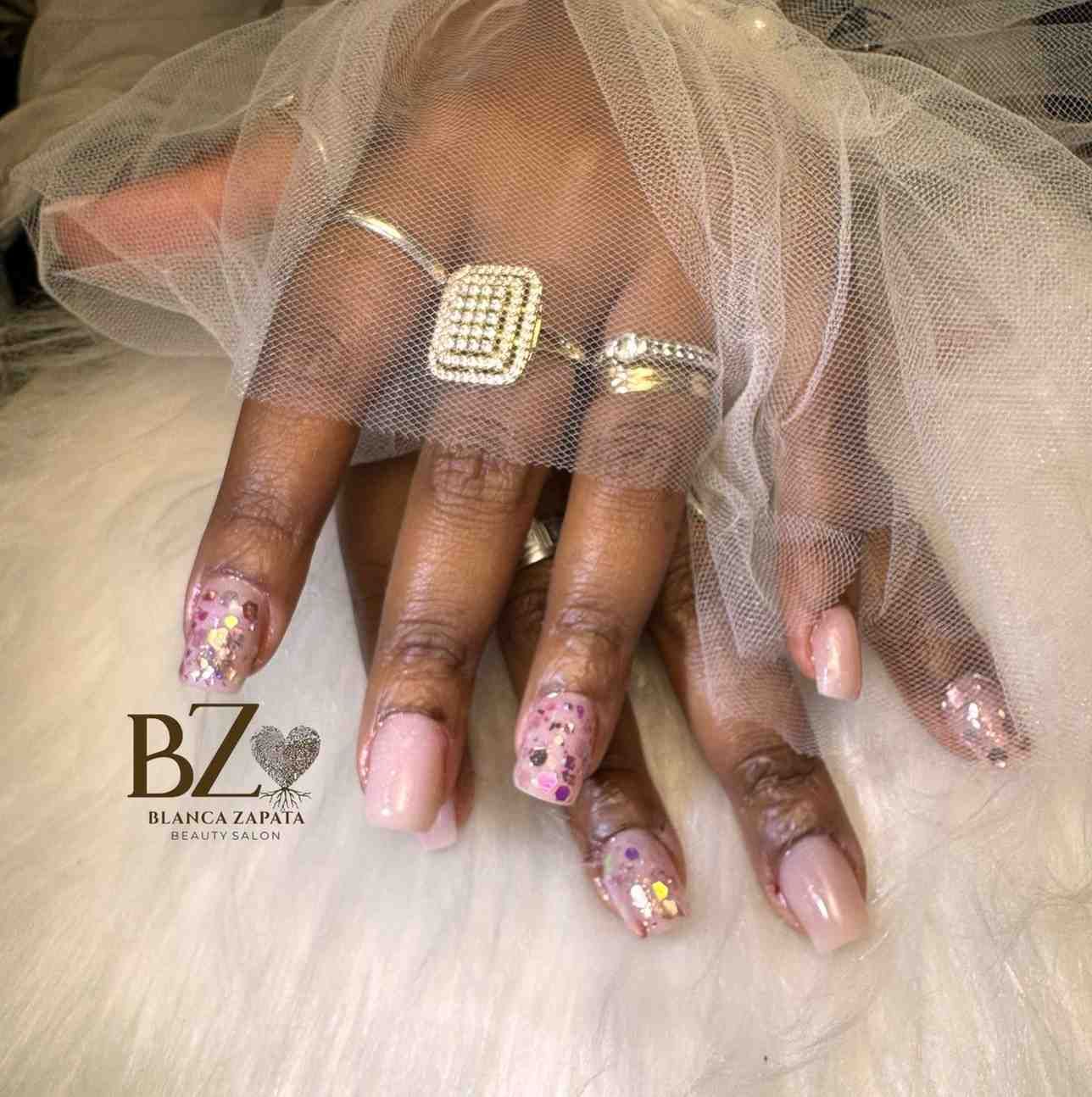 Mano con manicura rosa brillante y un anillo de diamantes de imitación bajo una tela blanca transparente.