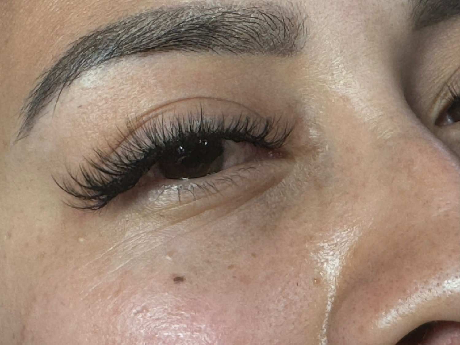 Primer plano de un ojo con largas pestañas postizas y un pequeño lunar en la mejilla.