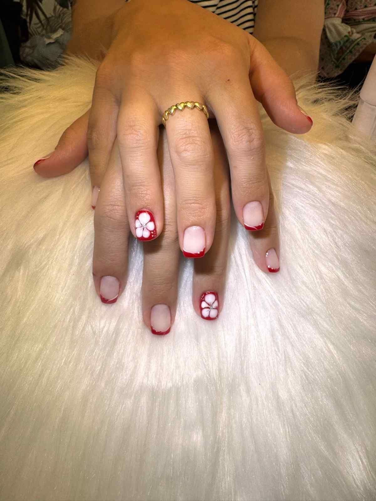Mano con manicura francesa y decoración de uñas con flores rojas descansando sobre un suave pelaje blanco.