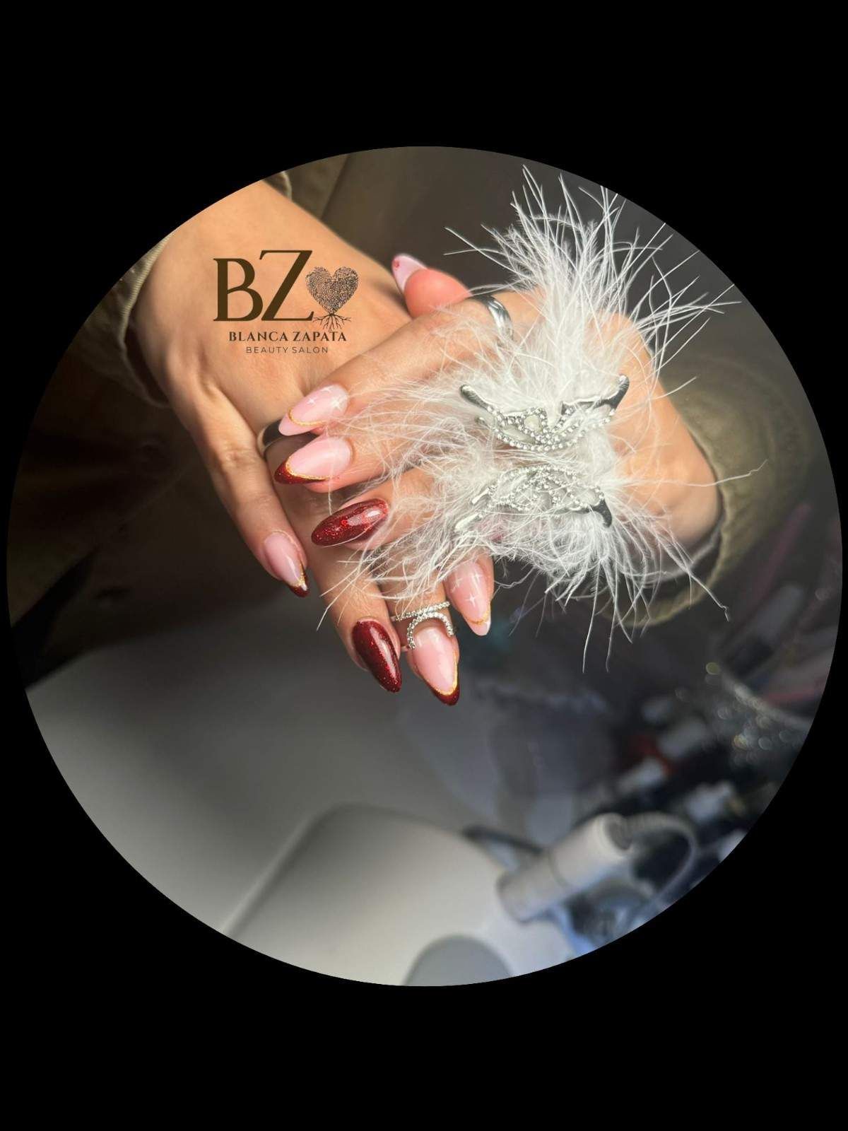 Manos con uñas color burdeos sosteniendo un accesorio blanco brillante con forma de pluma.