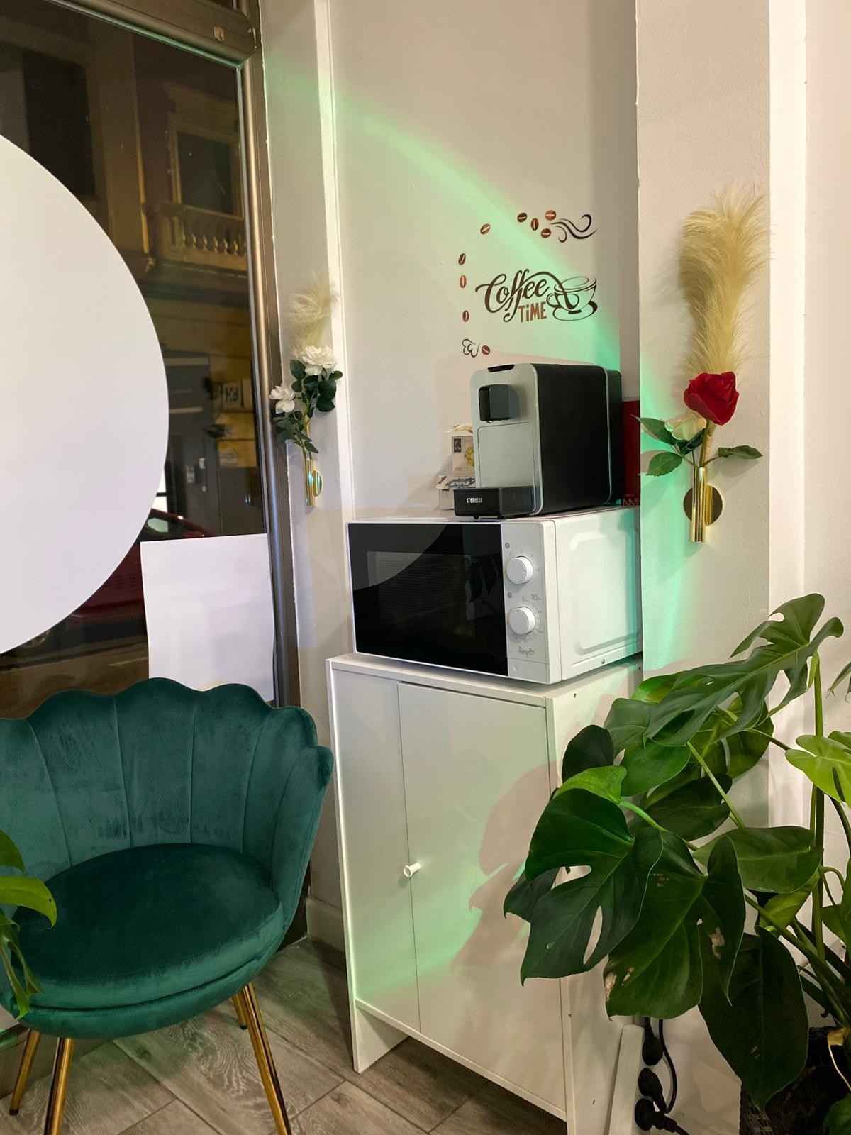 Sala de estar moderna con silla verde, armario blanco, microondas y un jarrón de flores en la pared.
