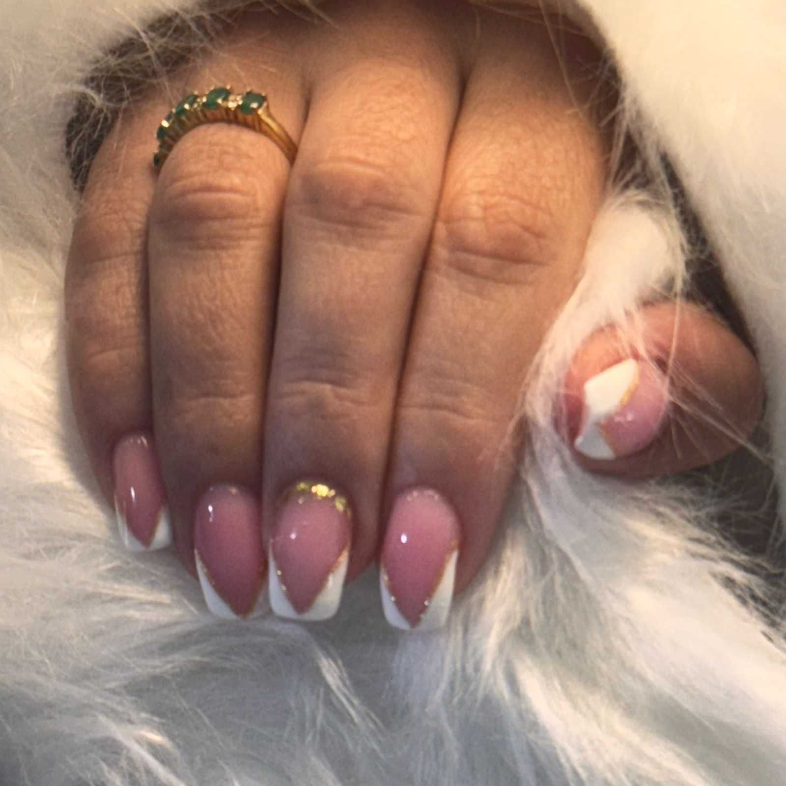 Mano con uñas pintadas de rosa con punta francesa y un anillo de oro descansando sobre piel blanca.