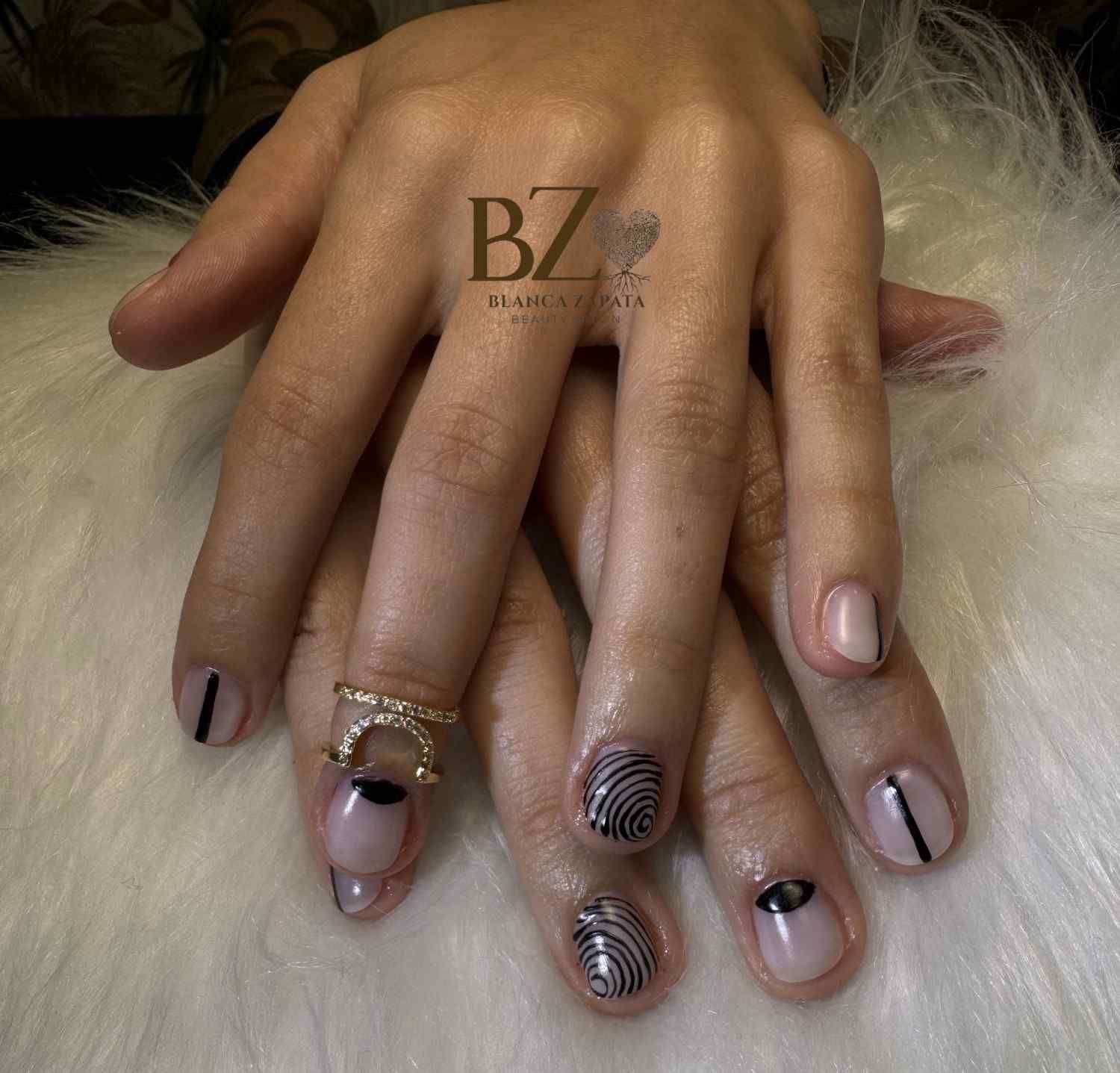 Mano con uñas decoradas en tonos nude y negro, descansando sobre piel blanca.