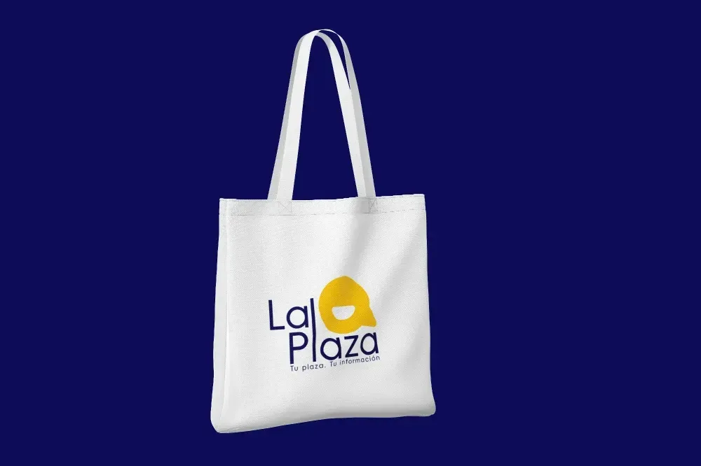 Bolso tote blanco con el logotipo de “La Plaza” sobre fondo azul.