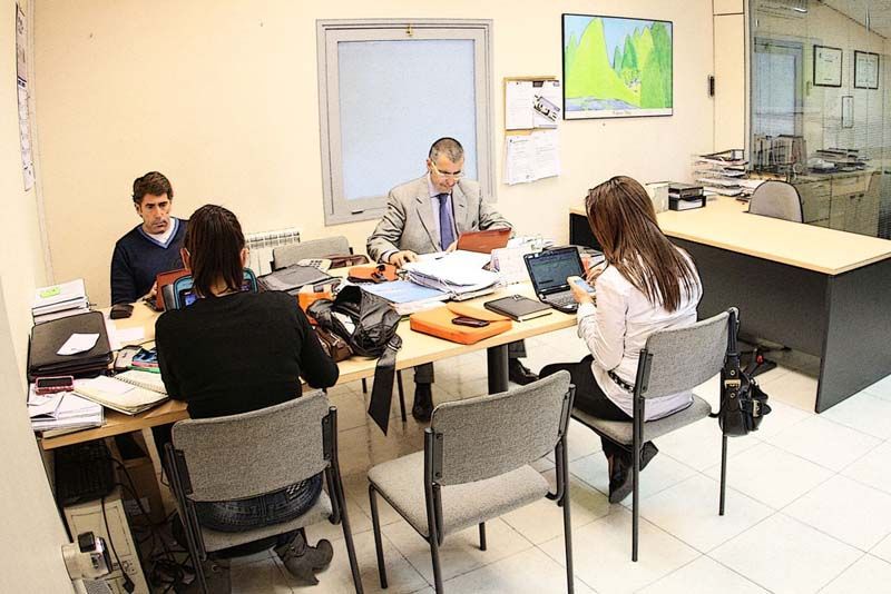 Cuatro personas en una mesa de oficina, trabajando con portátiles y papeles. Un hombre usa una tableta.
