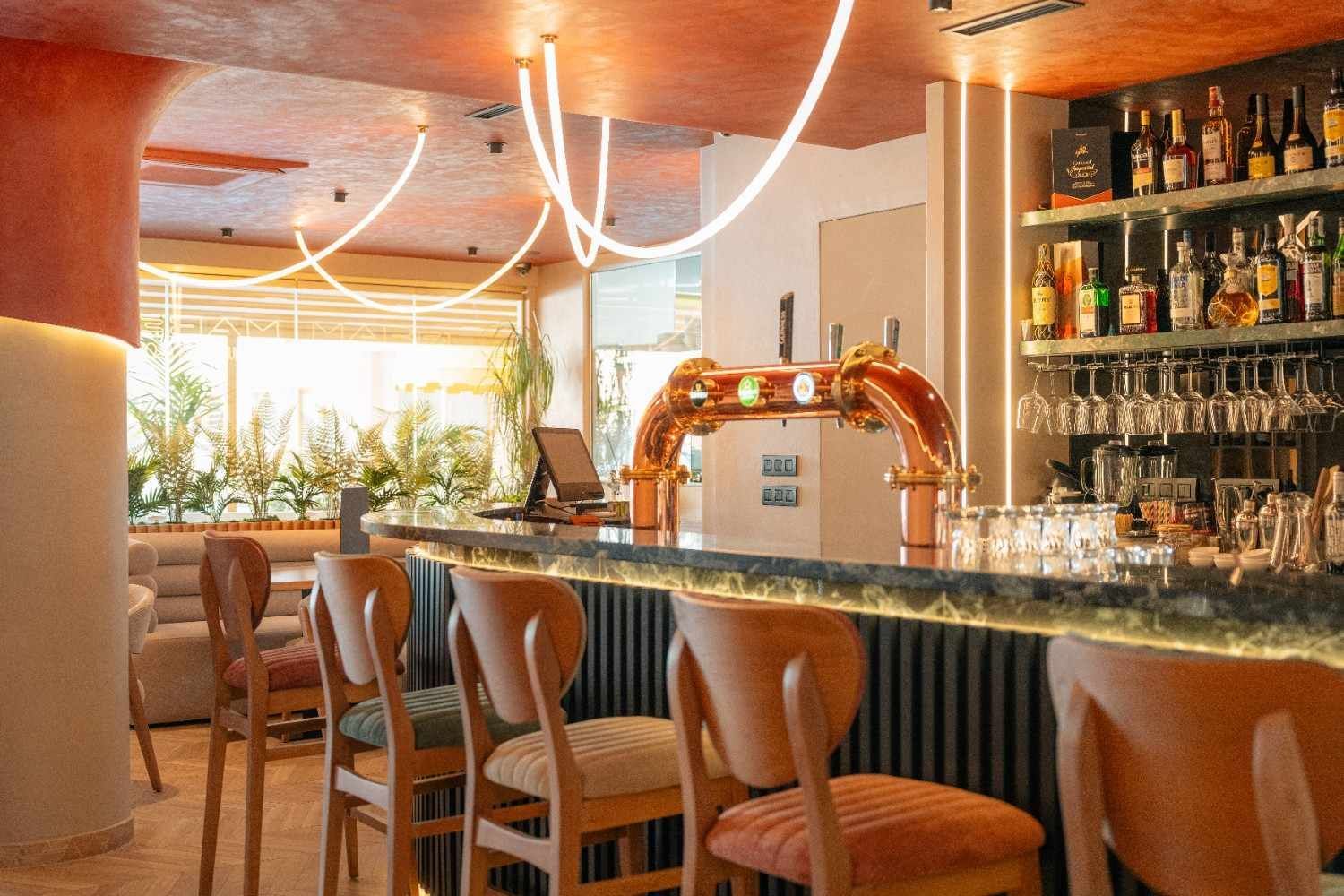 Elegante bar con mostrador de mármol, taburetes, iluminación cálida y estantes con licores detrás del mostrador.