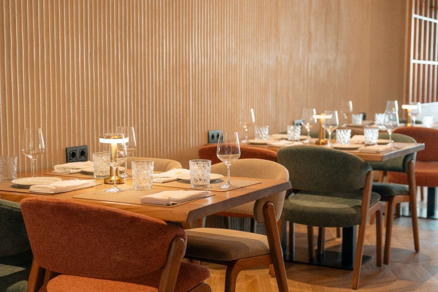 Elegante comedor de restaurante con mesas puestas, sillas verdes y paredes revestidas de cálidos paneles de madera.