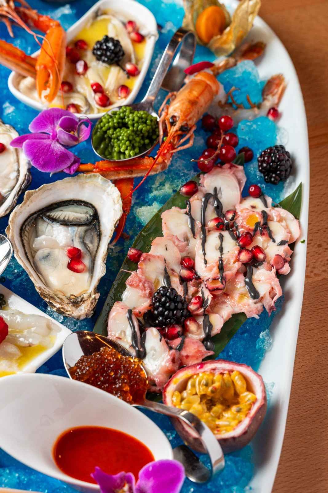 Plato de mariscos colorido con ostras, langosta, mejillones, bayas y salsa sobre una mesa blanca.