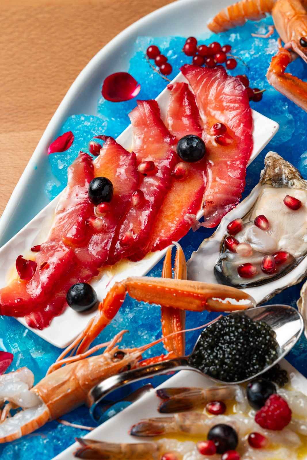 Plato de mariscos con ostras, camarones, patas de cangrejo y filetes de pescado rojo en un plato azul.
