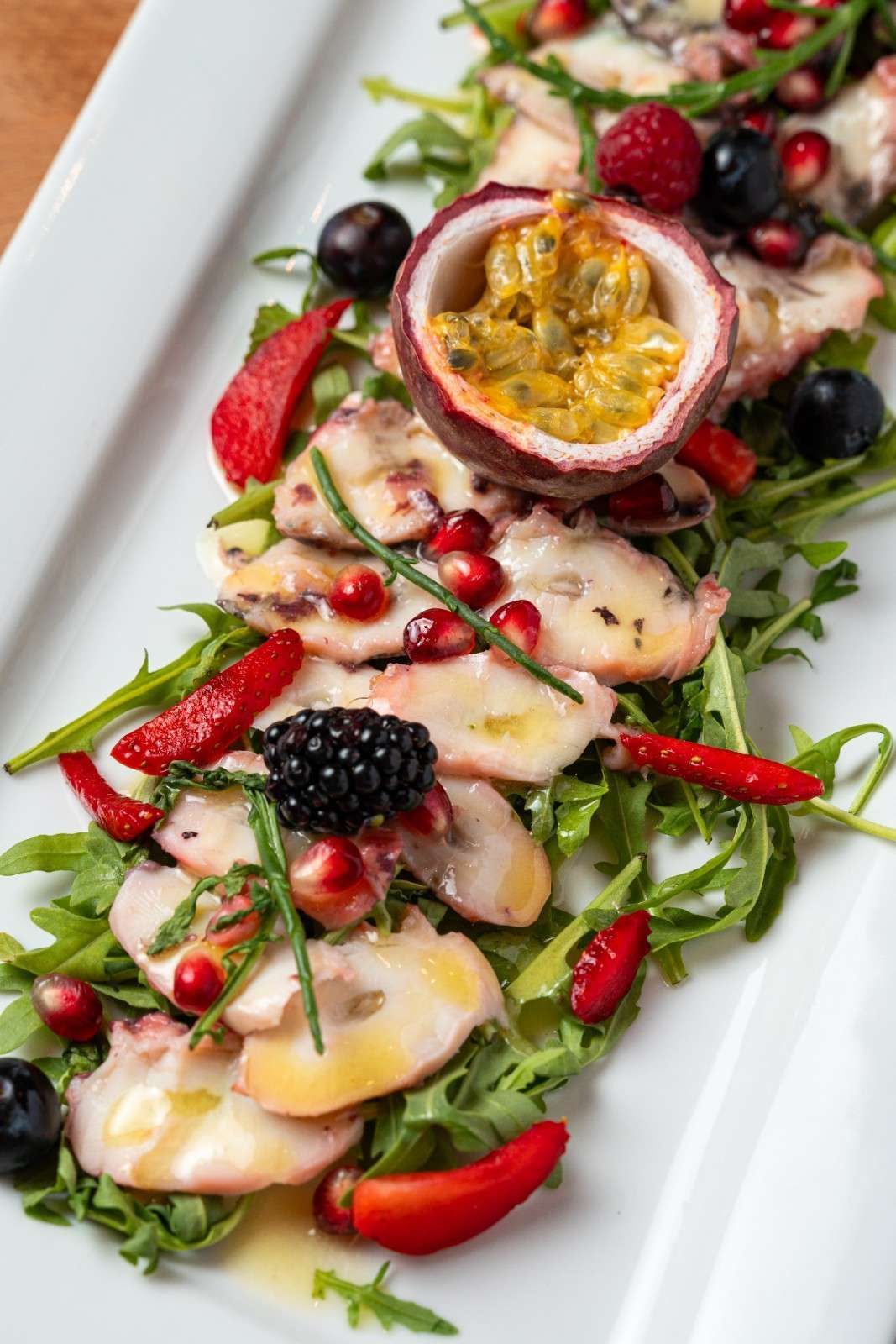Ensalada colorida de frutas y verduras con maracuyá, fresas, moras y semillas de granada en un plato blanco.