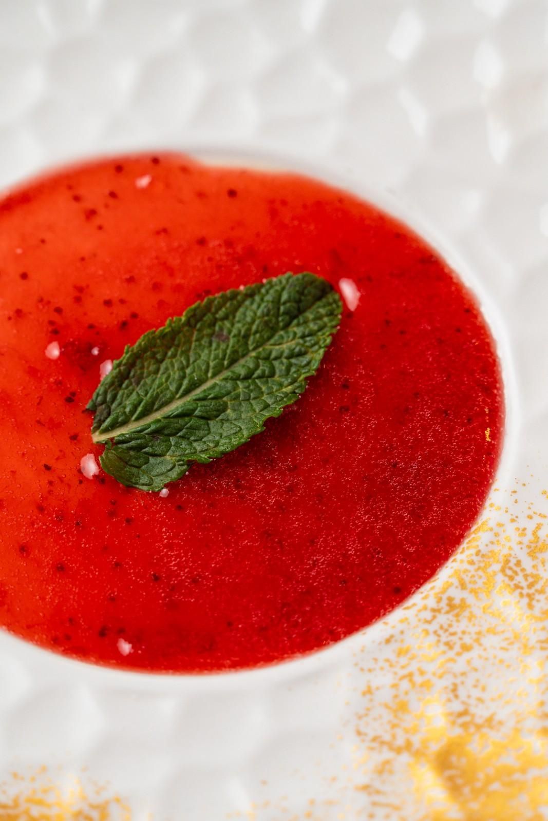 Sopa o salsa roja en un tazón blanco, coronada con una hoja de menta verde.