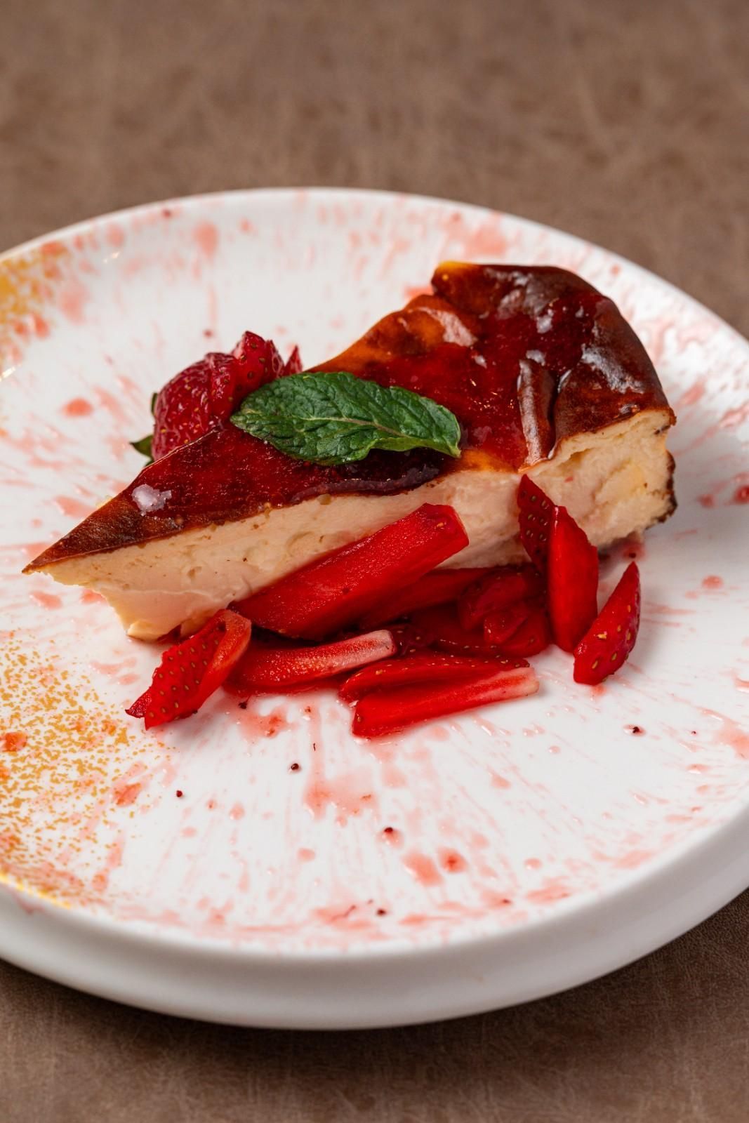 Porción de tarta de queso con salsa de fresa y fresas frescas en un plato blanco.