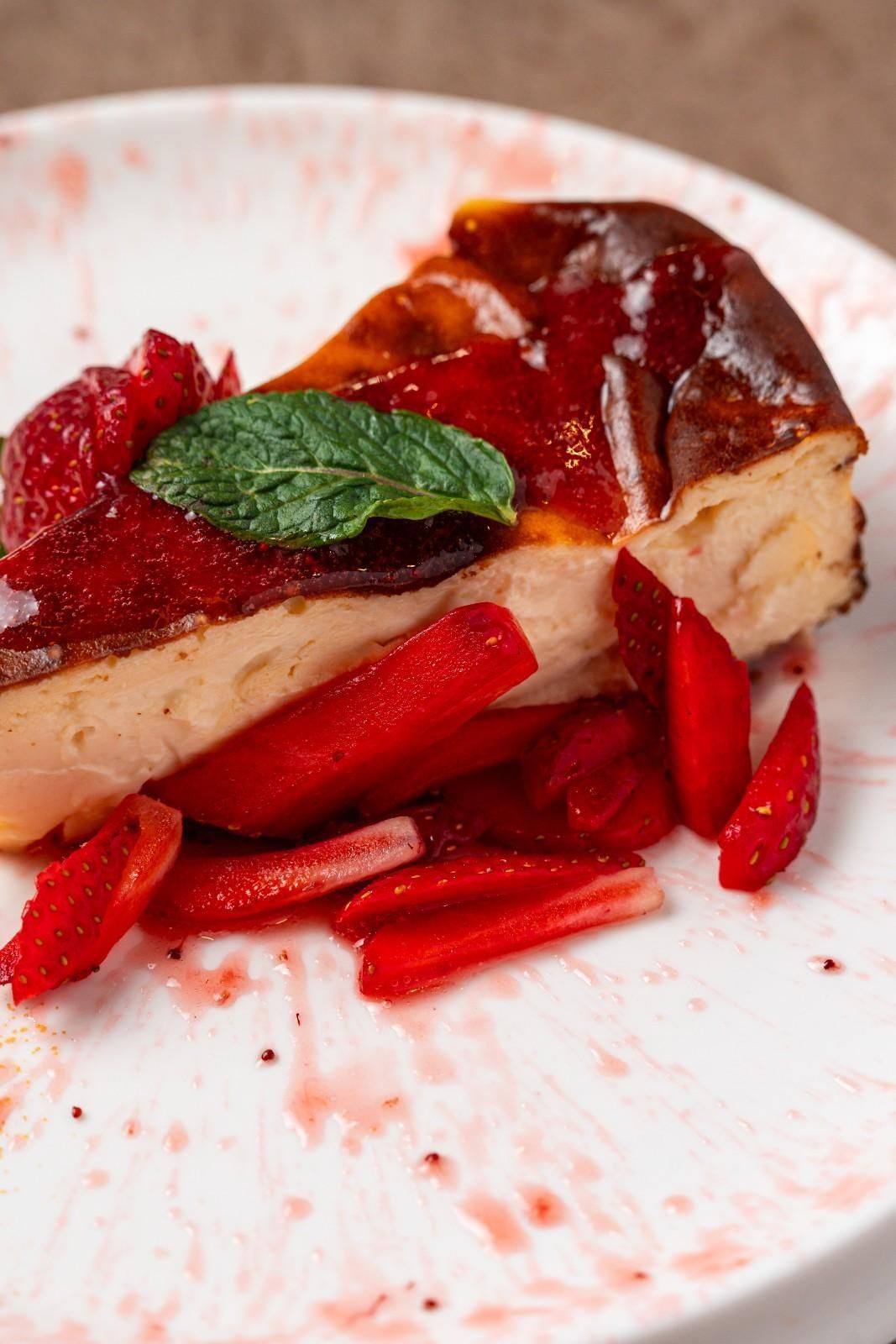 Porción de tarta de queso con fresas, cubierta con frutos rojos y menta, servida en un plato blanco.