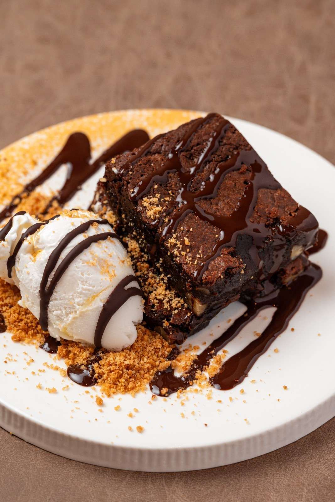 Porción de postre de chocolate con crema batida y sirope de chocolate sobre un plato blanco.