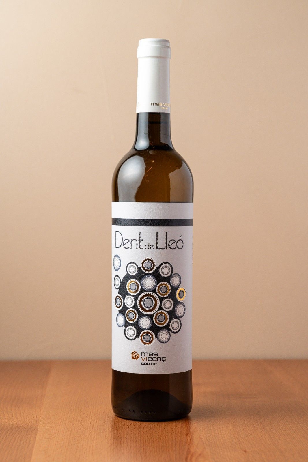 Botella de vino con etiqueta blanca y dibujo circular, colocada sobre una superficie de madera sobre un fondo beige.