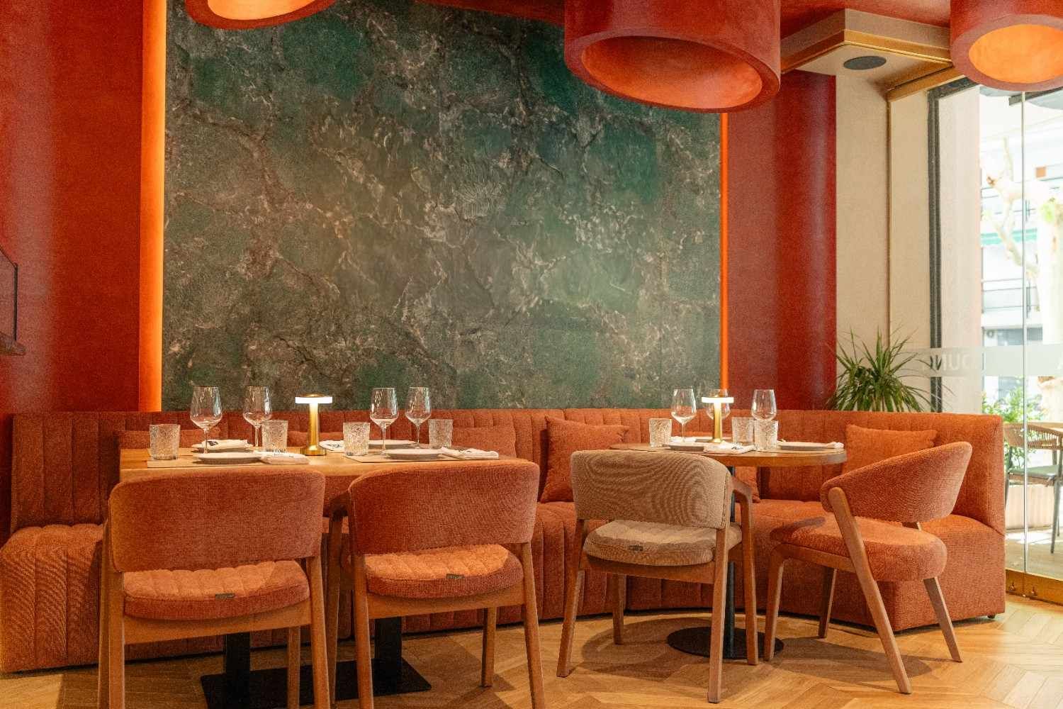 Acogedor reservado de restaurante con sillas naranjas, paredes rojas y una gran pizarra verde detrás de la mesa.
