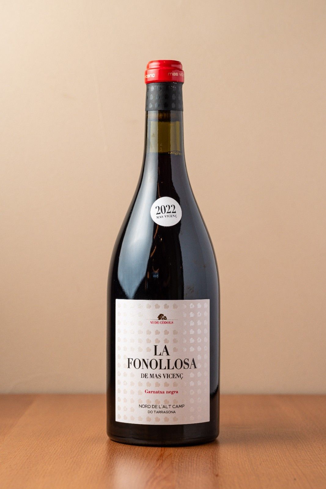 Botella de vino tinto La Revolución sobre una mesa de madera con fondo beige.
