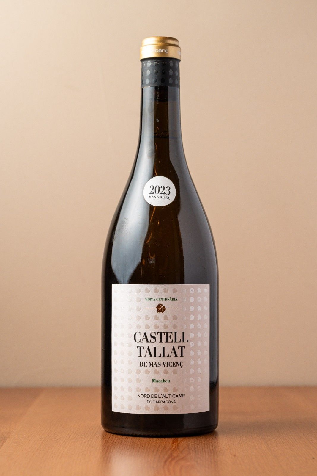 Botella de vino blanco Castello Tallai sobre una mesa de madera con fondo beige.