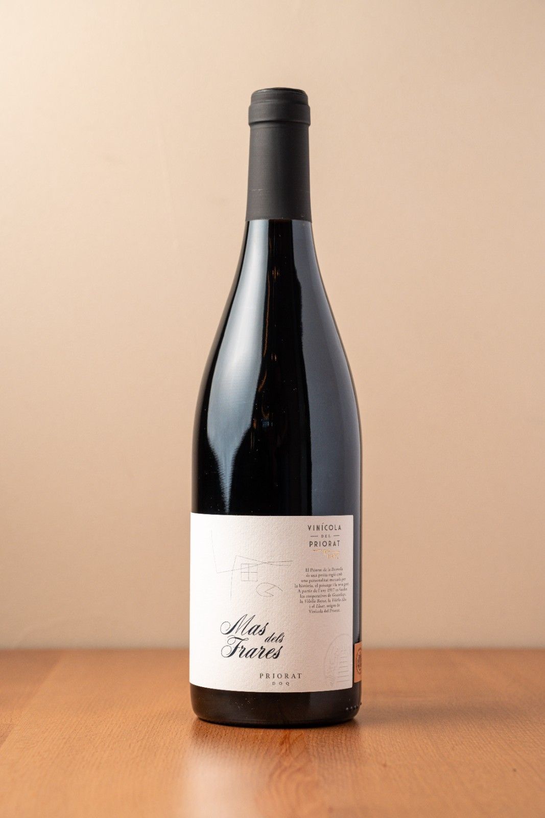 Botella de vino oscuro con etiqueta color crema sobre una mesa de madera con fondo beige.