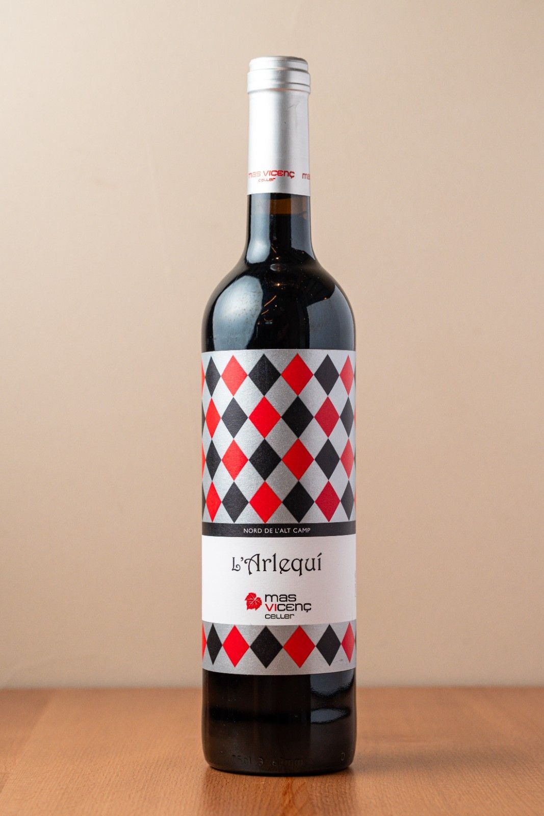 Botella de vino tinto con una etiqueta con un estampado de rombos rojos, blancos y negros sobre una mesa de madera.