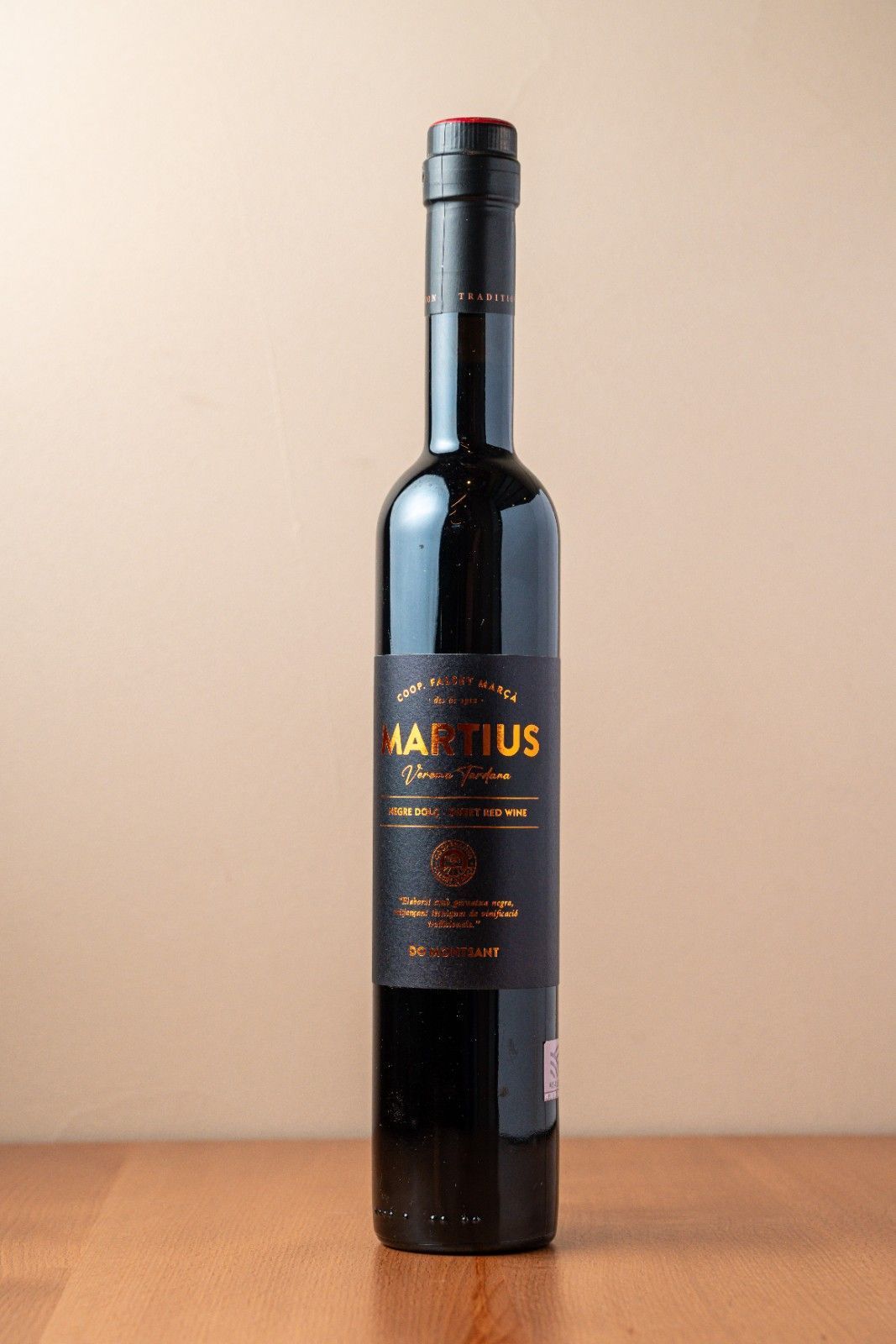 Botella de vidrio oscuro de vino tinto sobre una mesa de madera con fondo beige.