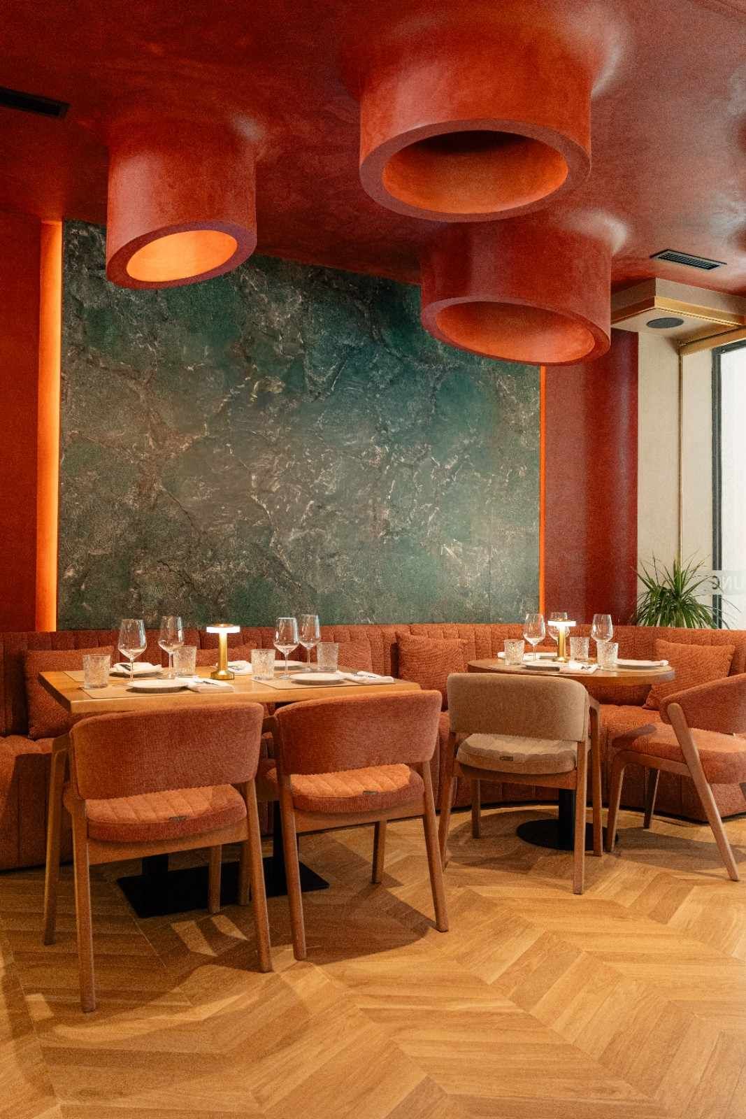 Interior cálido del restaurante con luces de techo naranjas, pared color turquesa, mesas de madera y sillas de mimbre.