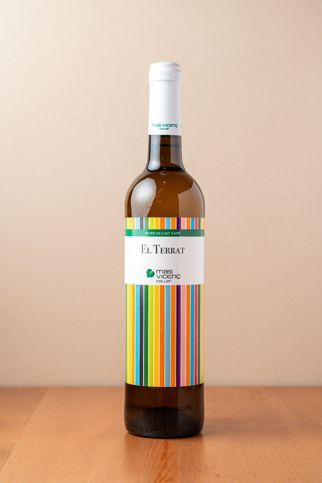 Botella de vino con etiqueta de rayas coloridas y tapón blanco sobre una mesa de madera.